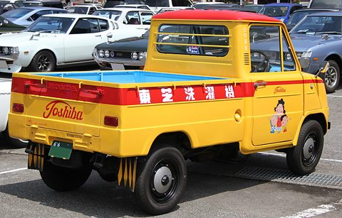 Rear three-quarter of a yellow pickup with a Toshiba script on the tailboard and a cartoon figure on the door. Opens a larger view