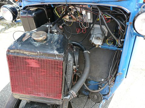 A red-cored radiator with a brass cap in front of a tangle of wiring and a small engine inside a blue nose. Opens a larger view