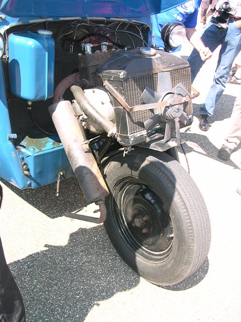 Close view under an open nose: a radiator, engine and exhaust mounted above a single front wheel.