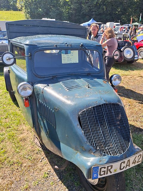 Front view of a faded blue three-wheeler with a mesh grille, one front wheel and plate GR CA 42. Opens a larger view