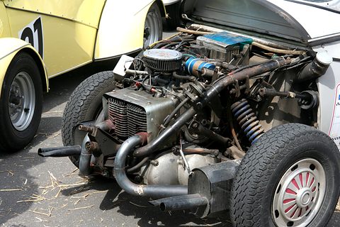 Exposed two-cylinder engine with exhaust pipes, coil-over springs and a rear wheel, the car’s body raised behind it. Opens a larger view