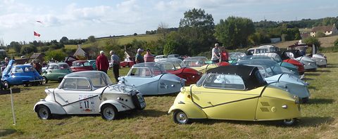 A field of small bubble cars under a wide sky, a white canopy Tg500 and a yellow soft-top Tg500 in the foreground. Opens a larger view