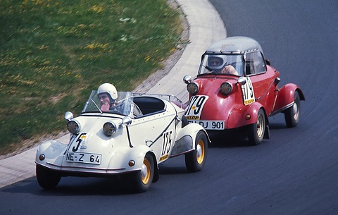 A white open Tg500 with a helmeted driver leads a red canopy Tg500 round a tight left-hand bend.