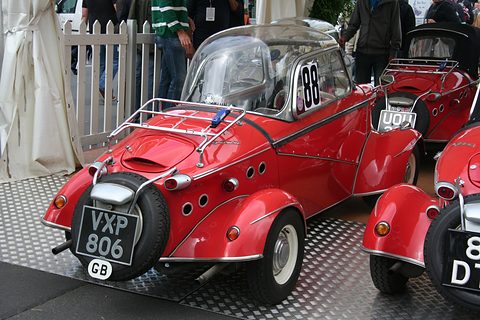 Red bubble car with its canopy raised, a luggage rack and a spare wheel with British plate VXP 806 on the tail. Opens a larger view