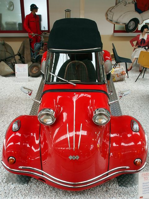Front of a red bubble car with a black hood, twin headlamps on bulbous wings and a chrome bumper bar. Opens a larger view
