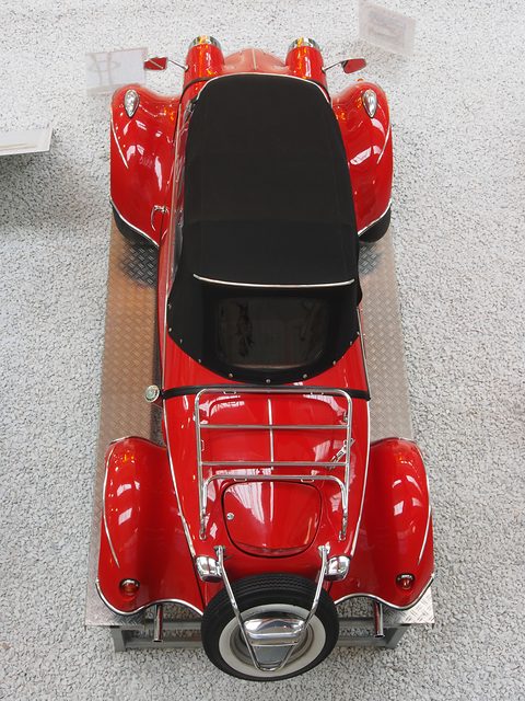 Overhead view of a red car with a black hood, its slim body tapering between two front and two rear wheels.