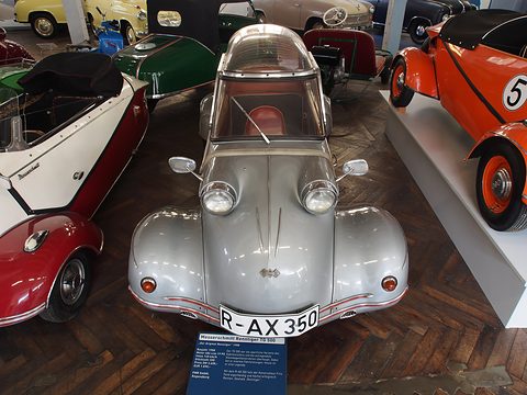 Front of a silver bubble car with twin headlamps on its wings and a canopy, an orange roadster numbered 5 beside it. Opens a larger view