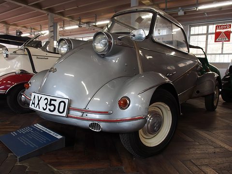 Silver bubble car with a clear canopy and red trim lines, plate R-AX 350, on a herringbone wooden floor. Opens a larger view