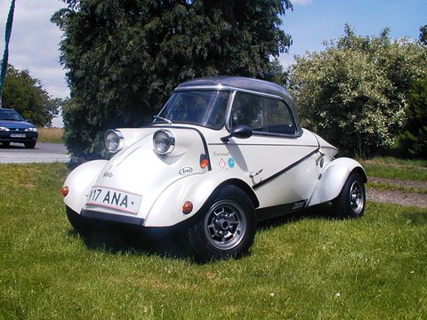 White bubble car with a dark tinted canopy, alloy wheels and sponsor decals, parked on grass by trees. Opens a larger view