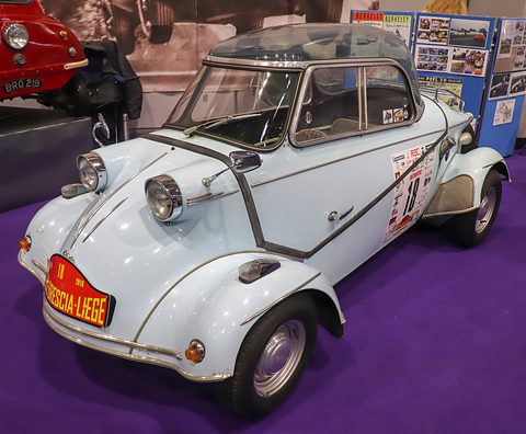 White bubble car with a canopy and red Brescia-Liège plate on its nose, rally decals on the door, on a purple carpet. Opens a larger view