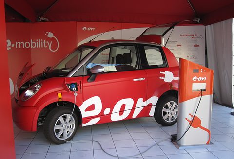 Red and white hatchback with a large e.on logo, plugged into an orange charging post in a red tent. Opens a larger view