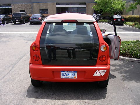 Rear of a red hatchback with a large dark glass tailgate, round tail lamps and a 100% badge in a car park. Opens a larger view