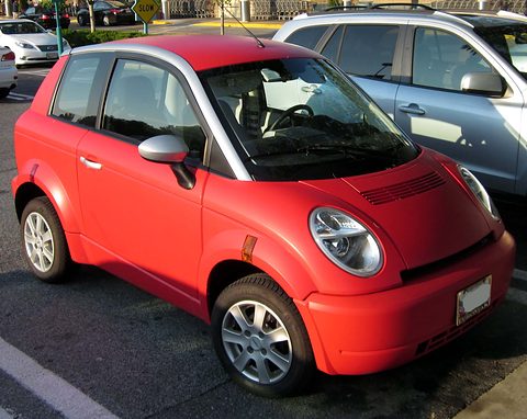 Red small hatchback with silver roof pillars and round headlamps parked beside a silver estate car. Opens a larger view