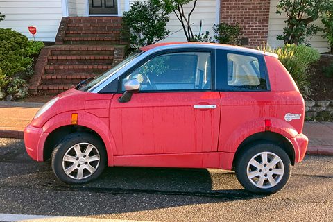 Side view of a faded red small hatchback with streaked paint and silver wheels in front of brick steps. Opens a larger view
