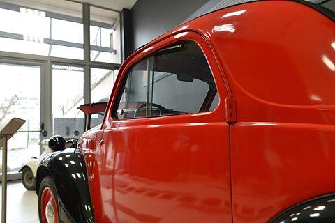 Close view of a glossy red door and black wing on a small car, a window behind. Opens a larger view