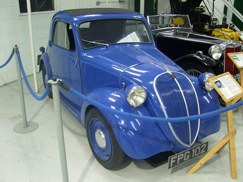 Bright blue small saloon behind a blue rope barrier, plate FPG 102, an information stand beside it. Opens a larger view