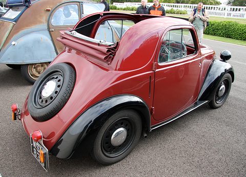 Red small car from the left rear, roof folded open, a spare wheel on the tail and a 2CV beside it. Opens a larger view
