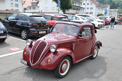 Maroon small saloon with a tall grille and wing-mounted headlamps in a car park. Opens a larger view