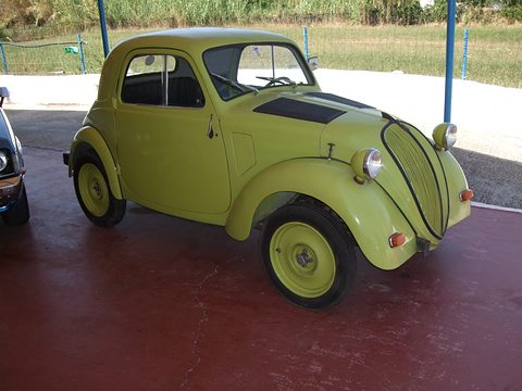 Lime-green small saloon with green wheels on a red concrete floor under a canopy. Opens a larger view
