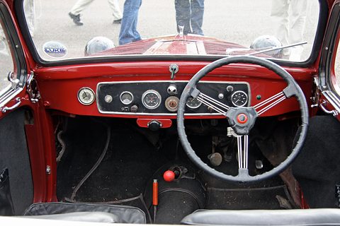 Red painted dashboard with a row of dials, a spring-spoke steering wheel and a floor gear lever. Opens a larger view