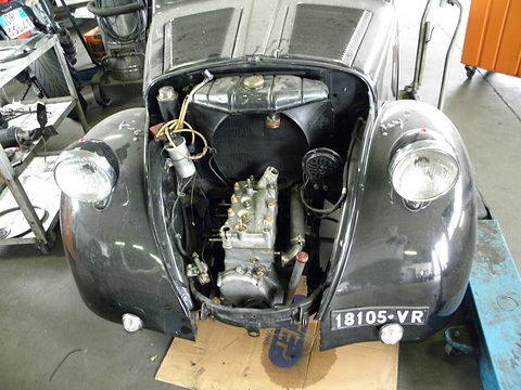 Front of a dark car with its bonnet up: four-cylinder engine ahead of the axle, radiator behind it. Opens a larger view