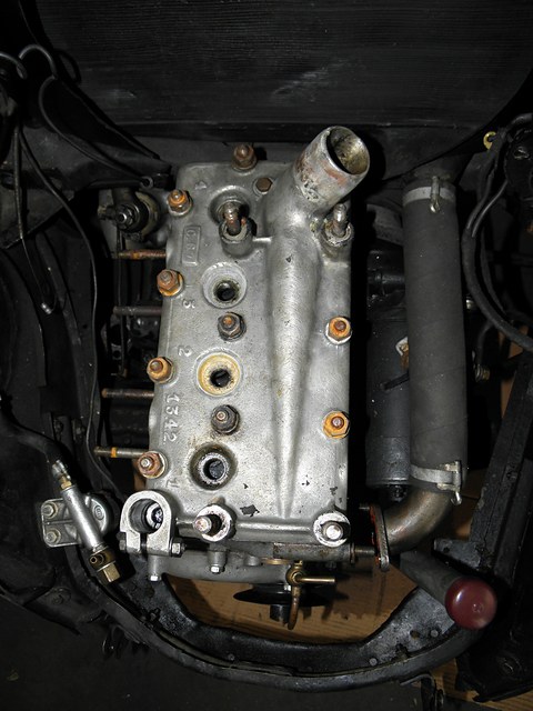 Aluminium cylinder head with spark plugs and pipework, seen from above in a dark engine bay. Opens a larger view