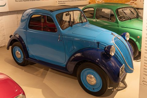 Blue small saloon with dark blue wings and an open roof, a green Topolino behind it. Opens a larger view