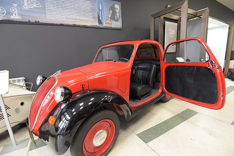 Red small saloon with its door swung open towards the rear, showing black seats inside. Opens a larger view