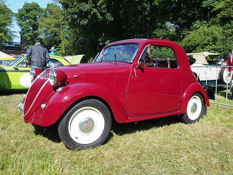 Red small saloon side-on on grass, white wheels and a rear-hinged door. Opens a larger view