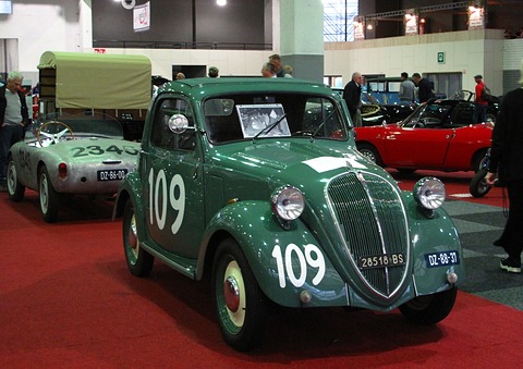 Green small saloon with white 109 numbers on its doors and bonnet, on a red carpet at a show. Opens a larger view