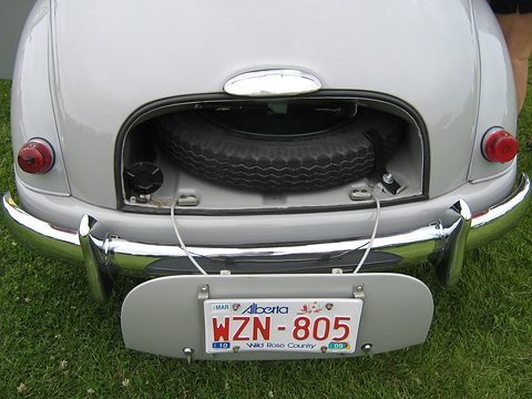 Rear of a pale grey car with its boot lid open showing the spare wheel, an Alberta plate below. Opens a larger view