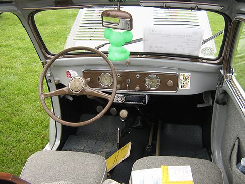Brown dashboard with two dials, a cream steering wheel and a green toy mouse hanging from the mirror. Opens a larger view