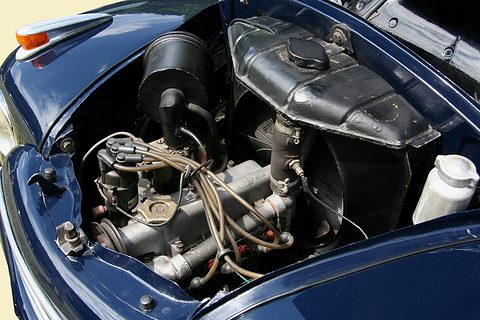 Engine bay under a navy bonnet: four-cylinder engine, coil, pipes and the radiator behind the engine. Opens a larger view