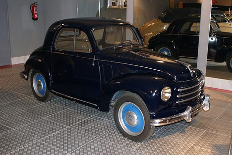 Dark blue small saloon with pale blue wheels on a chequered display floor. Opens a larger view