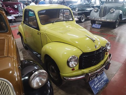 Yellow small saloon with a black grille and a blue museum plaque, other old cars around it. Opens a larger view