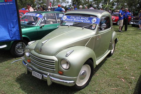 Pale green small saloon with a club sign on its windscreen, parked on grass among other cars. Opens a larger view