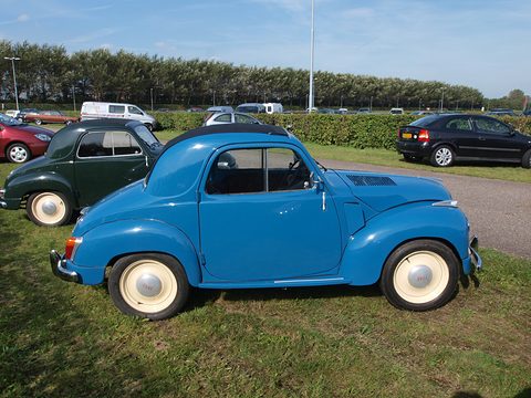 Blue small saloon side-on on grass, cream wheels and a black fabric roof, a green Topolino behind. Opens a larger view
