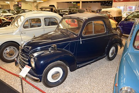 Navy small saloon with white wheels on a gravel display among other cars. Opens a larger view