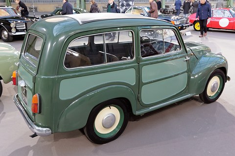 Green small estate with lighter side panels from the left rear on a sale floor. Opens a larger view