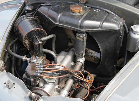 Engine bay with the four-cylinder engine, coil, carburettor and copper pipes, radiator behind. Opens a larger view