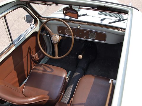Brown leather seats, a thin steering wheel and a brown dashboard seen through the open door. Opens a larger view