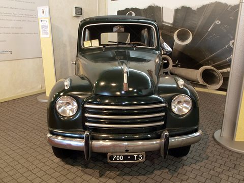 Dark green small estate from the front with a horizontal-bar grille and plate 700 TS, museum panels behind. Opens a larger view