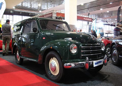 Dark green small van with cream wheels on a red show carpet, visitors behind. Opens a larger view