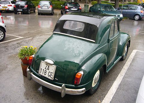 Dark green small car from behind on wet tarmac, its fabric roof closed and an Italian plate on the tail. Opens a larger view