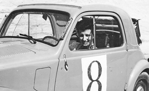 Black and white: a smiling woman behind the wheel of a small saloon with a number 8 on its door. Opens a larger view