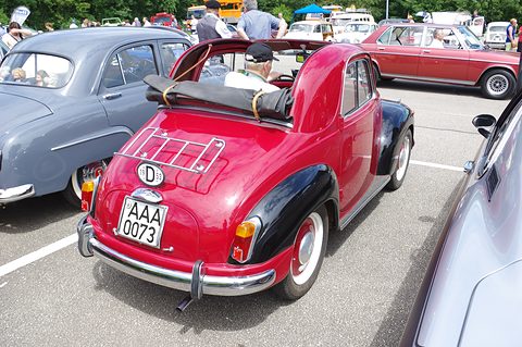 Red small saloon from the left rear with black wings, a luggage rack on the tail and its roof folded. Opens a larger view