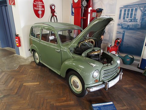 Green small estate with its bonnet up in a museum display with a petrol-station mannequin behind. Opens a larger view