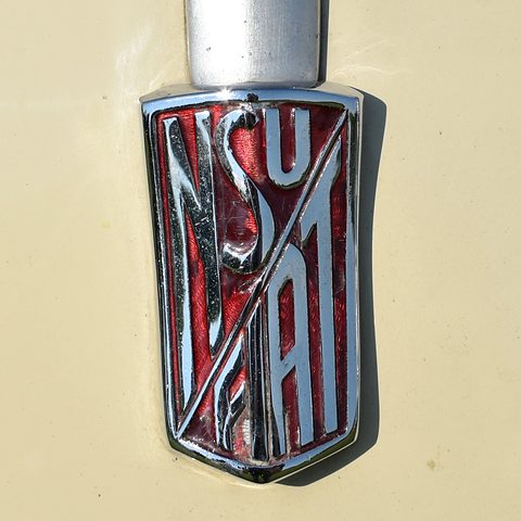 Chrome shield with interlaced red NSU and FIAT lettering on cream paint. Opens a larger view