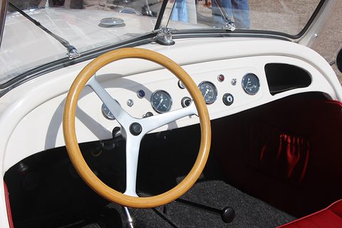 White dashboard with small round dials and a wood-rimmed three-spoke steering wheel. Opens a larger view