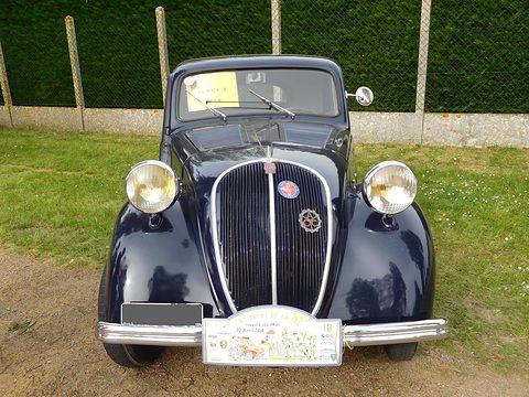 Front of a navy small saloon: tall grille with a badge, wing-mounted headlamps and a rally plaque. Opens a larger view
